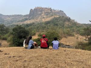 three people sitting on a hill looking at a mountain at Misty Falls Karjat Waterfall view in Jambrung  +20 photos
