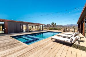 a swimming pool with two lounge chairs on a wooden deck at Iconic 7,000sf Glass Villa with 2 Pools on 350 Acres in Pioneertown