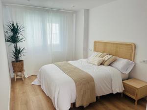 a white bedroom with a large bed and a plant at RÍA LIVING - Arena 01 in Cee