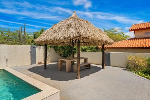 a picnic table and a straw umbrella next to a swimming pool at Salinja Cerca 2-B in Palm-Eagle Beach
