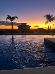 a pool with palm trees and a sunset in the background at Cantinho Solis in Itupeva