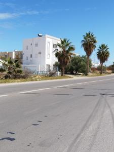 an empty street with palm trees and a white building at Djerba Haven Family in Houmt Souk