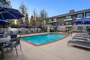 a swimming pool with chairs and blue umbrellas at Howard Johnson by Wyndham Fullerton/Anaheim Conference Cntr in Fullerton