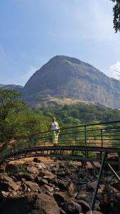 a woman standing on a bridge with a mountain in the background at Home Stay in Arogyam at Mulshi Backwaters in Mulshi