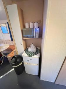 a small room with a microwave and a trash can at Seawick Beach Caravan in Saint Osyth +3 photos