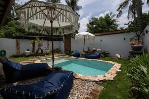 a pool with chairs and an umbrella in a yard at The Swan Villa in Gili Trawangan