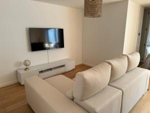 a white living room with a white couch and a tv at Sea Breeze - Espinho Beach in Espinho