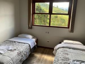 two twin beds in a room with a window at Pousada Cantinho da Montanha 2 in Visconde De Maua