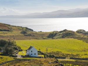 a white house in a green field with the ocean at Aird House in Ardfern