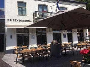 Eine Gruppe von Tischen und Stühlen mit einem Sonnenschirm vor einem Gebäude in der Unterkunft Hotel De Lindeboom in Den Burg