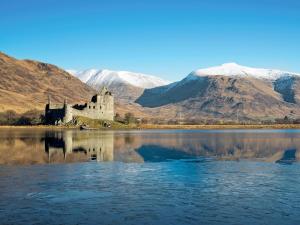 a castle in the middle of a lake with mountains at Blackmill Cottage in Taynuilt +2 photos