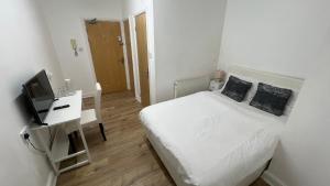 a small white bedroom with a bed and a television at Sangha Hall - Private Ensuite Rooms with Shared Kitchen in Leicester