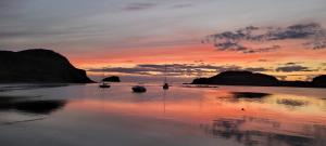 a sunset with boats in the water on a beach at Crimson Sky Cottage in Twillingate