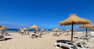 a beach with chairs and straw umbrellas and the ocean at Casa da Cortiça in Seixal