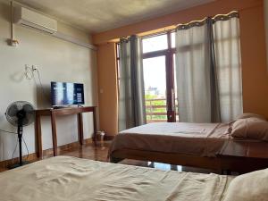 a bedroom with two beds and a window with a television at Heliconia's Inn in Puerto Maldonado