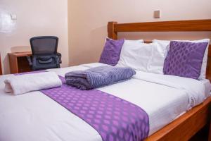 a bed with purple and white sheets and a chair at Kaisa Gardens in Nairobi