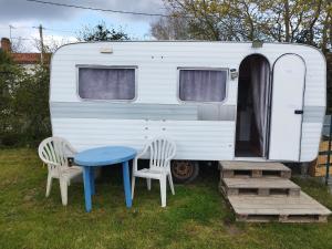 two chairs and a table in front of a caravan at Caravane cocooning in Saint-Martin-des-Noyers