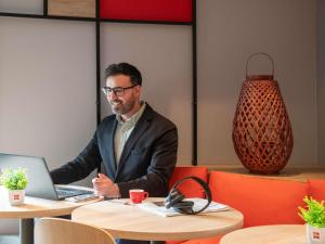 a man in a suit sitting at a table with a laptop at Ibis Roquebrune Cap Martin Menton in Menton
