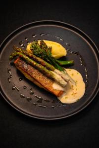 ein schwarzer Teller mit einem Stück Fisch und Spargel in der Unterkunft Molėtairesort in Molėtai