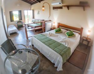 a bedroom with a bed with a glass table and a chair at Pousada Alem das Formas in Carrancas