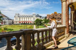 a woman standing on a balcony looking at a building at La Villa L'Argentine in Cabourg