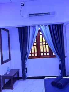 a bedroom with a blue curtain and a window at Clara's Beach Inn in Trincomalee