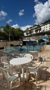 a white table and chairs next to a pool at Ap Centro - Wi-fi, Piscina, com Vista da Praça in Águas de Lindoia