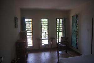 a room with three windows and a table and a chair at Laguna Lodge in Ouidah