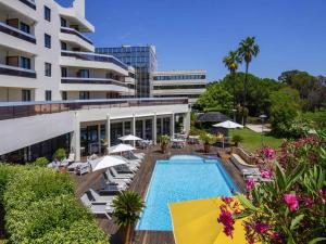 an outdoor swimming pool with chairs and umbrellas next to a building at Mercure Hyères Centre Côte d'Azur in Hyères
