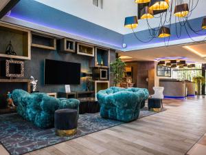 a living room with two blue chairs and a flat screen tv at Novotel Orléans Saint Jean de Braye in Saint-Jean-de-Braye