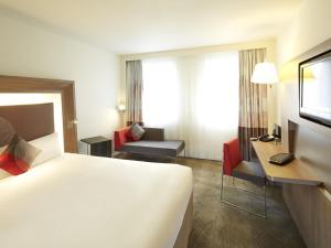 a hotel room with a large white bed and a desk at Novotel Mechelen Centrum in Mechelen