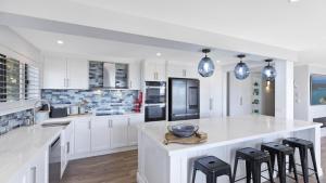 a white kitchen with white cabinets and black appliances at Avoca Dream in Avoca Beach