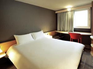 a bedroom with a large white bed and a red chair at ibis Criciuma in Criciúma +86 photos