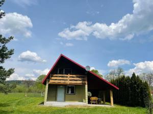 a small house with a red roof on a field at Domek nad Wiarem in Huwniki