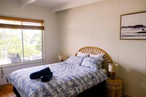 a bedroom with a bed with blue sheets and a window at Sanctuary Spaces - Wategoes Beach Shack in Byron Bay