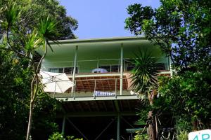 a green house with a balcony with an umbrella at Sanctuary Spaces - Wategoes Beach Shack in Byron Bay