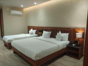 two beds in a hotel room with white sheets at Shreeja Central in Bhawānipatna