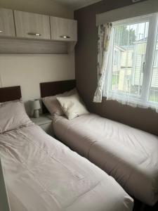 two beds in a room with a window at Beach Retreats, Romney Sands, Parkdean Resorts in Greatstone
