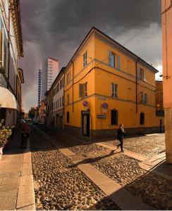 a woman walking down a cobblestone street next to a yellow building at Locanda dell Angelo in Piacenza