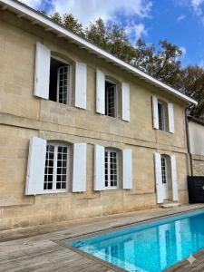 a building with white shuttered windows and a swimming pool at La Chartreuse du Château La Garde in Martillac