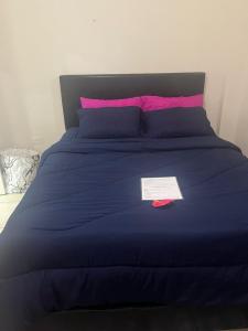 a blue bed with pink pillows and a paper on it at Cozy Modern flat in Tunapuna