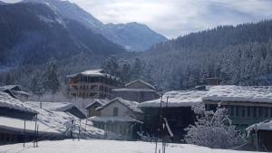 a group of buildings with snow covered roofs and mountains at Himalayan bite pulga in Kalgha