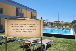 a sign in front of a swimming pool with chairs at Hotel 3K Faro Aeroporto in Faro