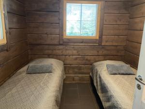two beds in a room with wooden walls and a window at Villa Nuttu - Loppusiivous kuuluu hintaan in Jämsä