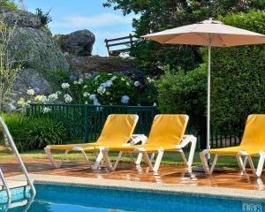 drei Stühle und ein Sonnenschirm neben einem Pool in der Unterkunft Hotel & Apartamentos Cons da Garda in San Vicente de O Grove