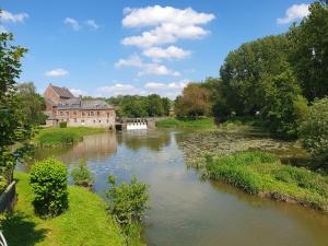 a river in front of a large building and a building at Les Mout'Anes in Saint-Hilaire-sur-Helpe