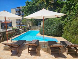 a pool with chairs and umbrellas next to a swimming pool at Apartamentos Casa da Pedra in Ubatuba