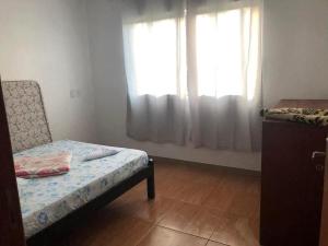 a small room with a bed and two windows at Riba House in Imbituba