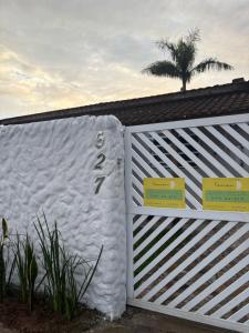 a white fence with a palm tree in the background at Apê Mini Casa - Ar condicionado - ao lado do Sesc Bertioga dentro da Pousada Lemon in Bertioga