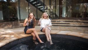 two women sitting on a bench next to a swimming pool at Architectual Design, Plunge Pool, Lagoon Frontage in Pearl Beach